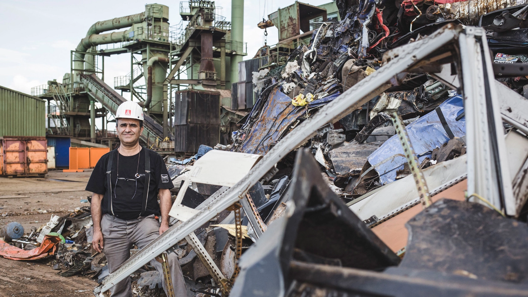 Betriebsrat Ayhan Yalgin steht auf dem Gelände der DEUMU umgeben von Bergen Metallschrott