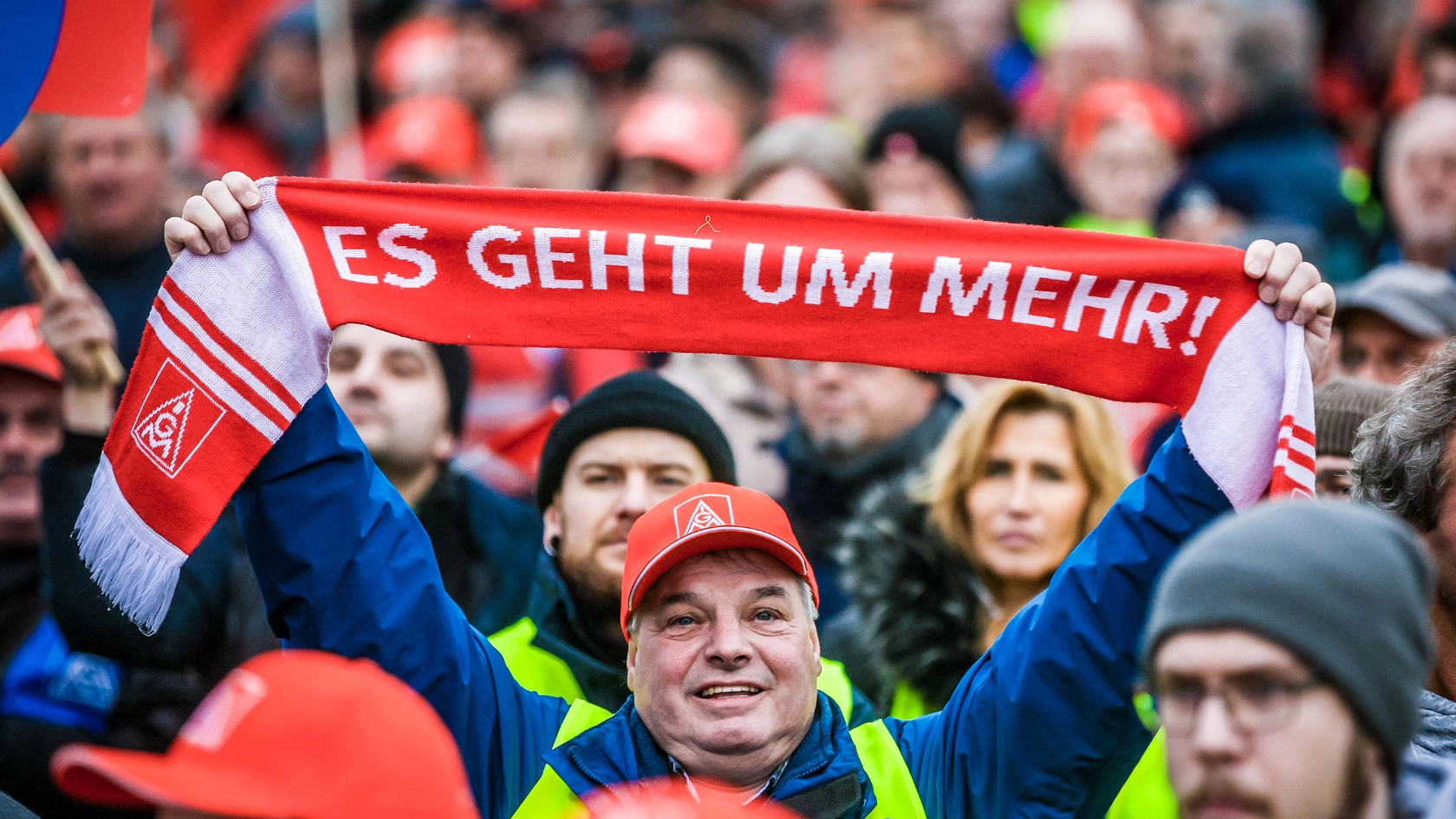Mann in einer Menschenmenge hält einen Schal mit der Aufschrift "Es geht um mehr!" in die Höhe.