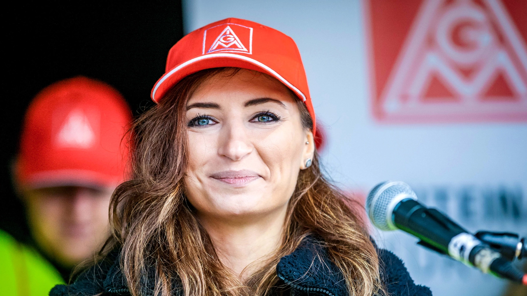 Eine Frau mit langem braunem Haar und IG Metall-Kappe blickt lächelnd in die Kamera.