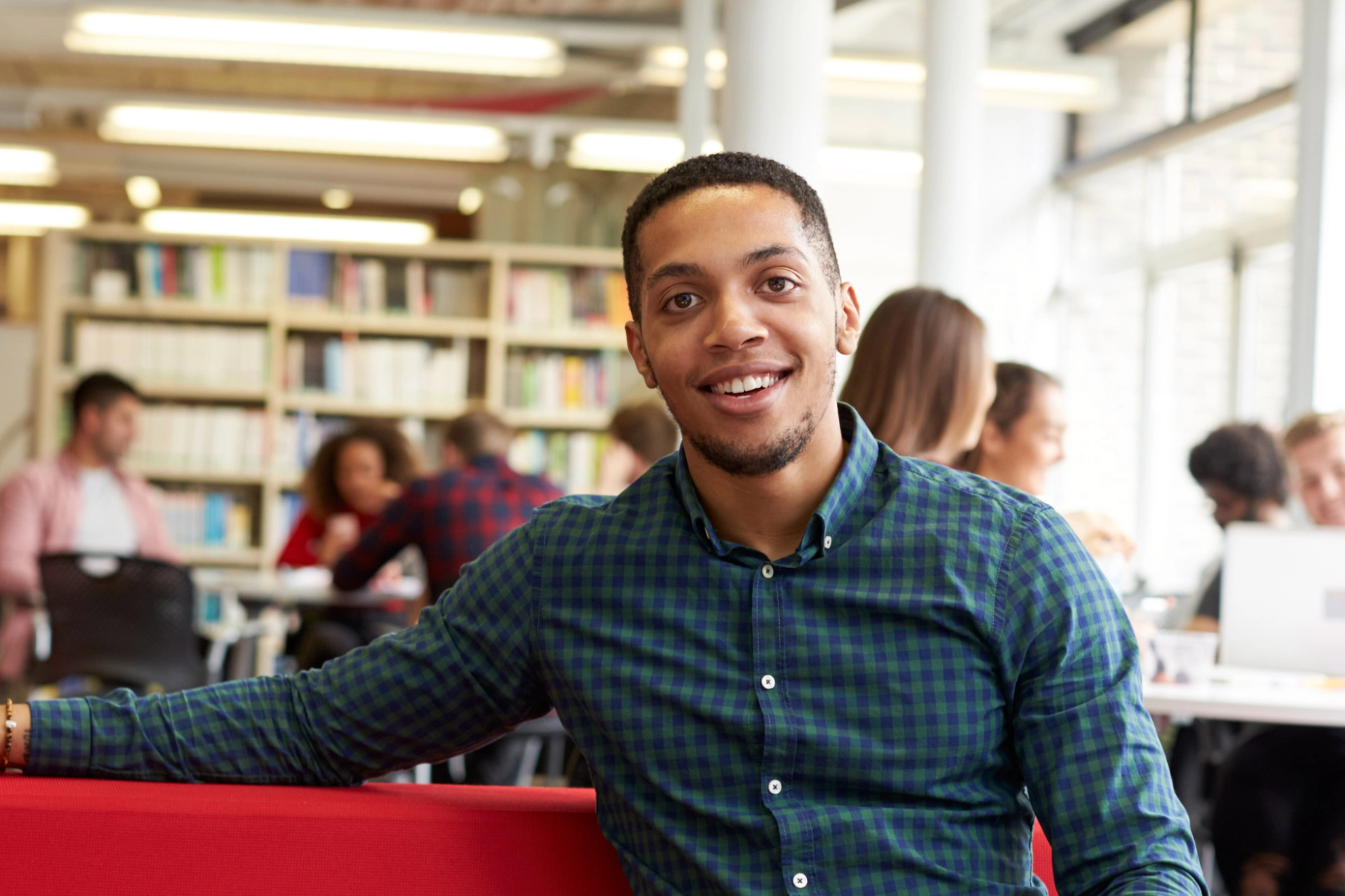 Student sitzt in der Bibliothek auf einem roten Sofa.