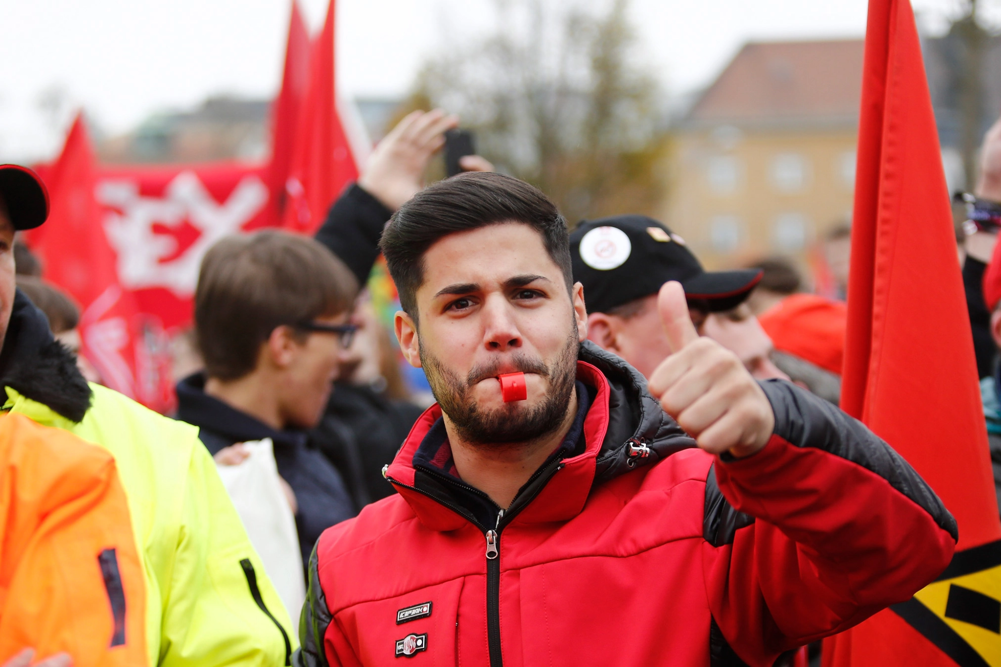 Ein junger Mann mit roter Jacke und Trillerpfeife streckt den Daumen nach oben.