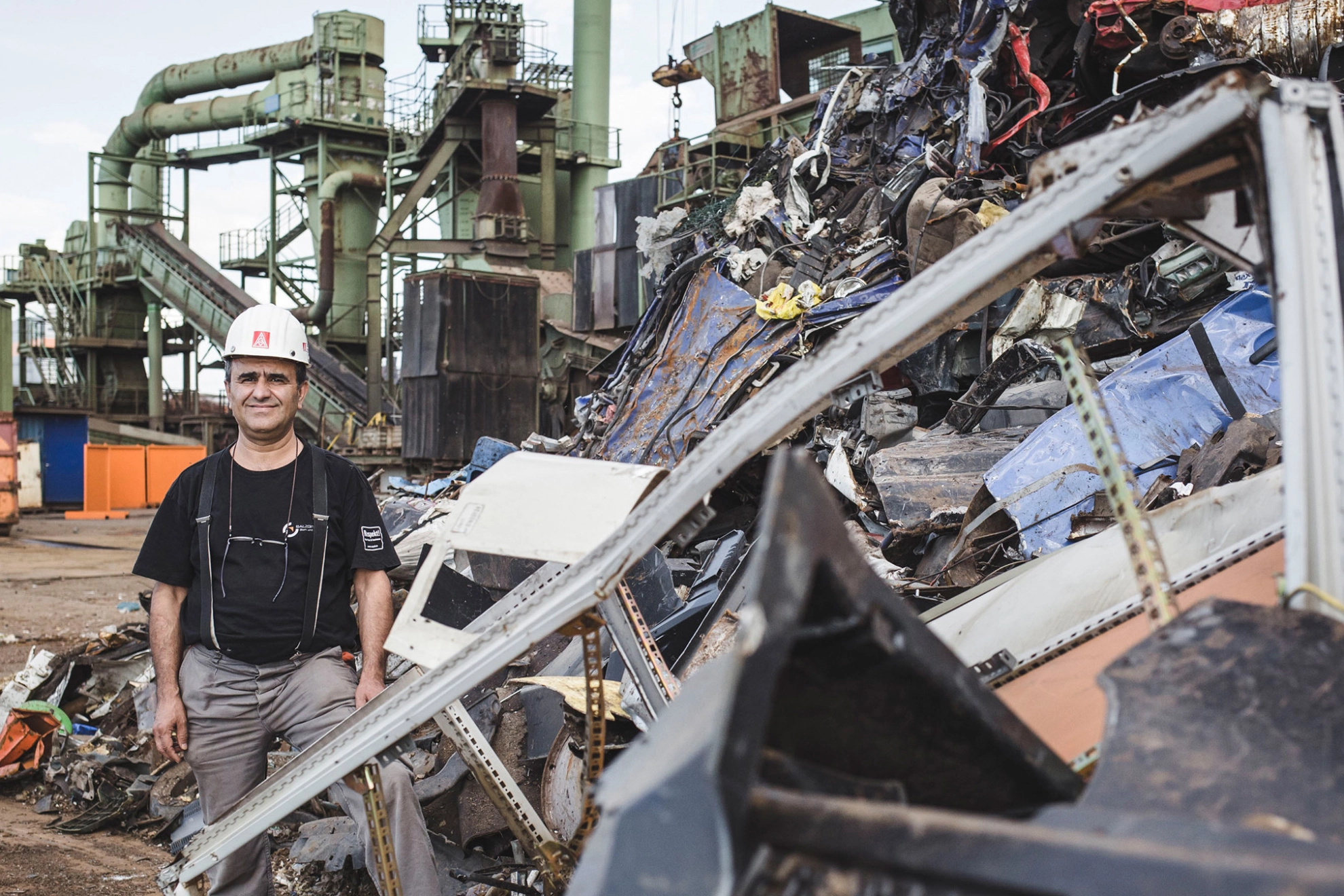 Betriebsrat Ayhan Yalgin steht auf dem Gelände der DEUMU umgeben von Bergen Metallschrott