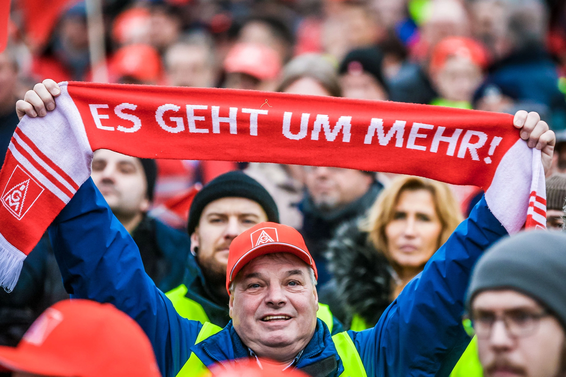 Mann in einer Menschenmenge hält einen Schal mit der Aufschrift "Es geht um mehr!" in die Höhe.