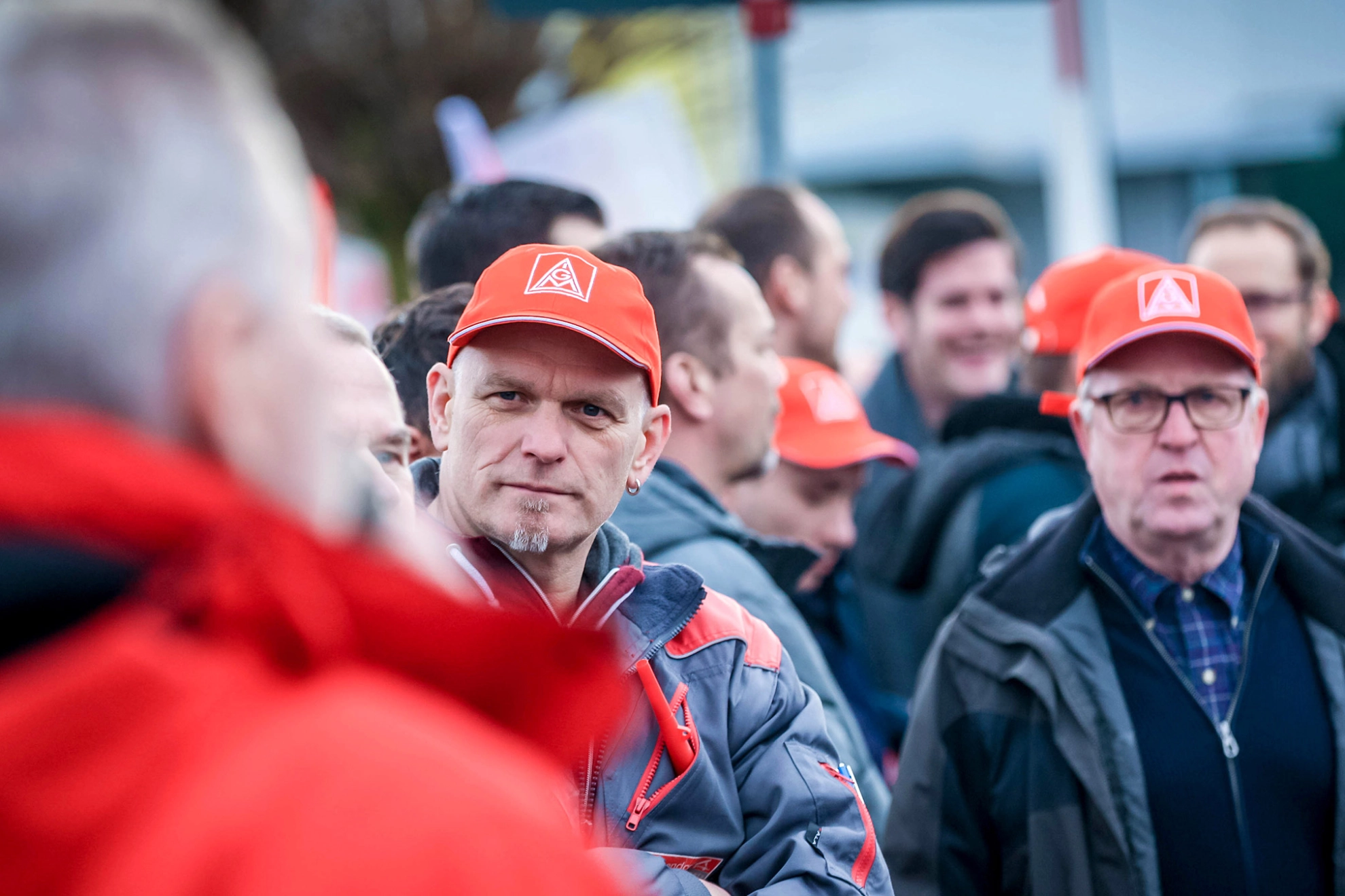 Ein Mann mit Arbeitsjacke und roter Kappe blickt in das Gesicht eines Mannes am Bildrand.