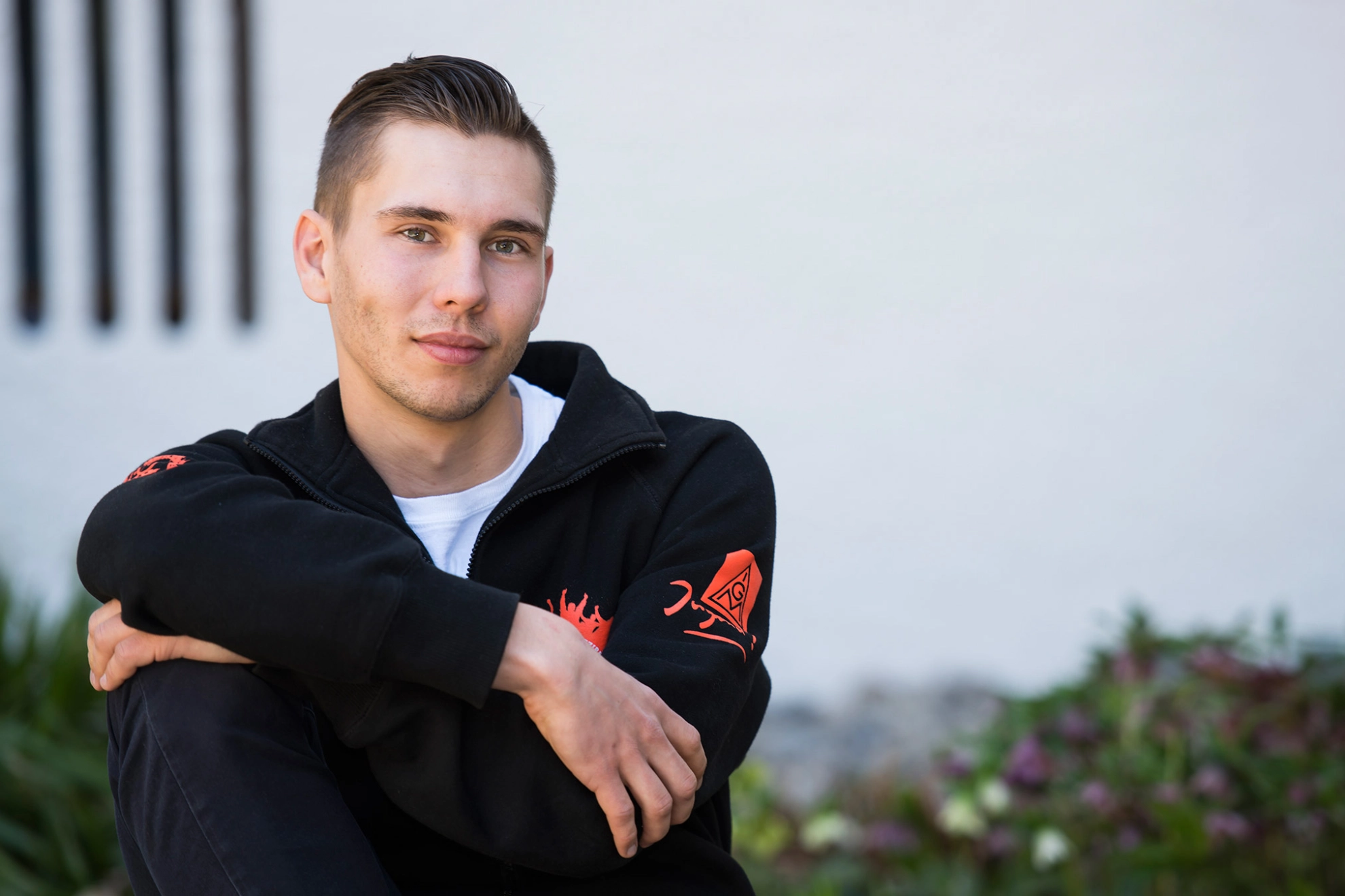 Junger Mann mit IG Metall Jugend-Jacke blickt mit verschränkten Armen direkt in die Kamera.