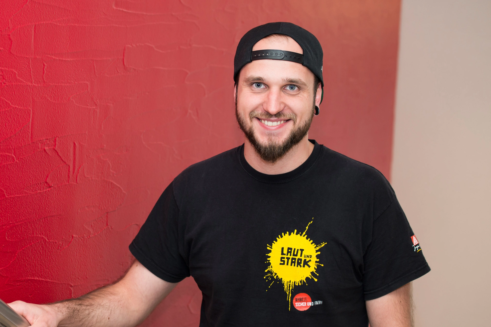 Junger Mann mit IG Metall-Kampagnen-Shirt blickt lächelnd direkt in die Kamera.