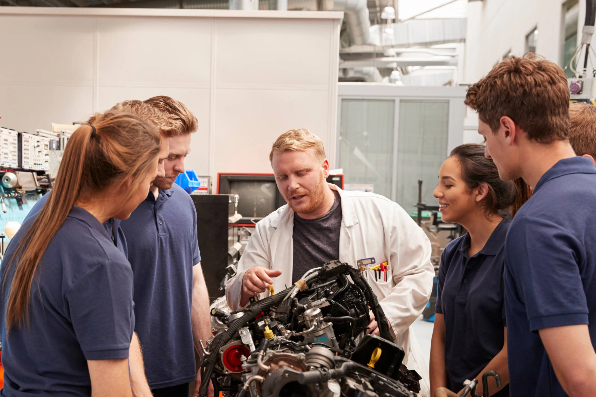 Auszubildende und Ausbilder stehen um einen Motor herum.