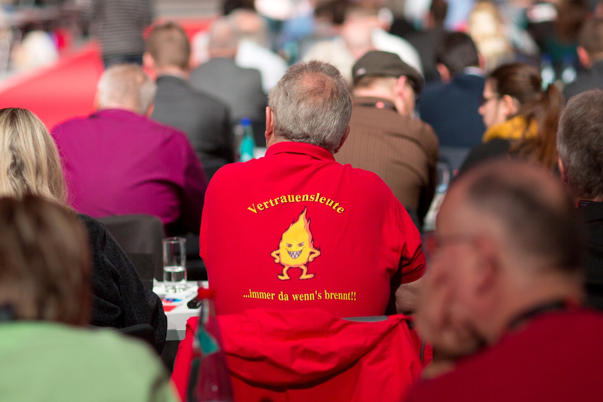 Mann auf einer Konfernez von hinten in einem roten Pulli.