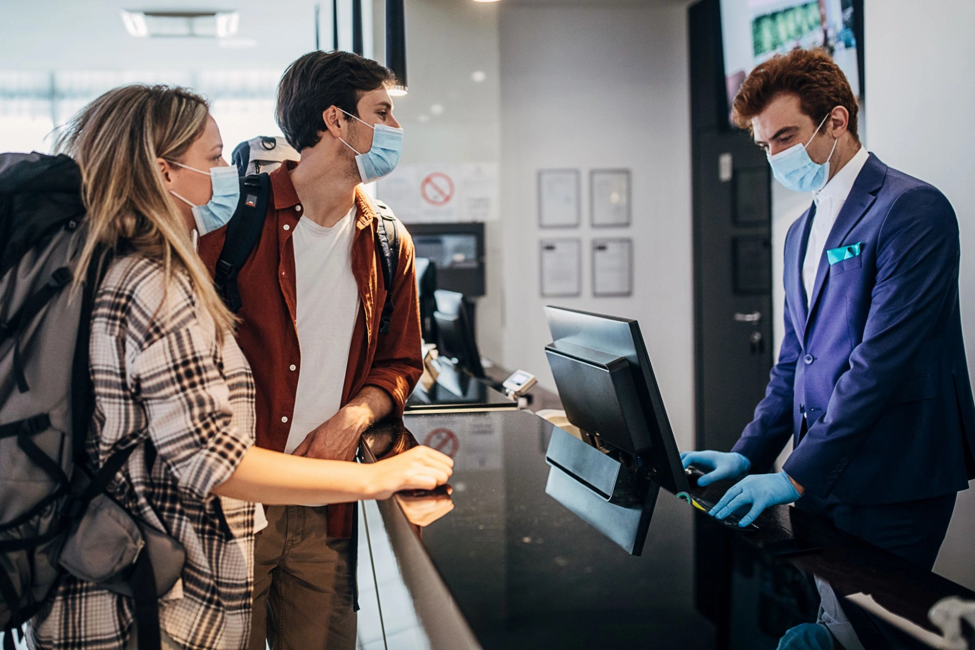 Paar trägt schützende Gesichtsmaske beim Check-in an der Hotelrezeption