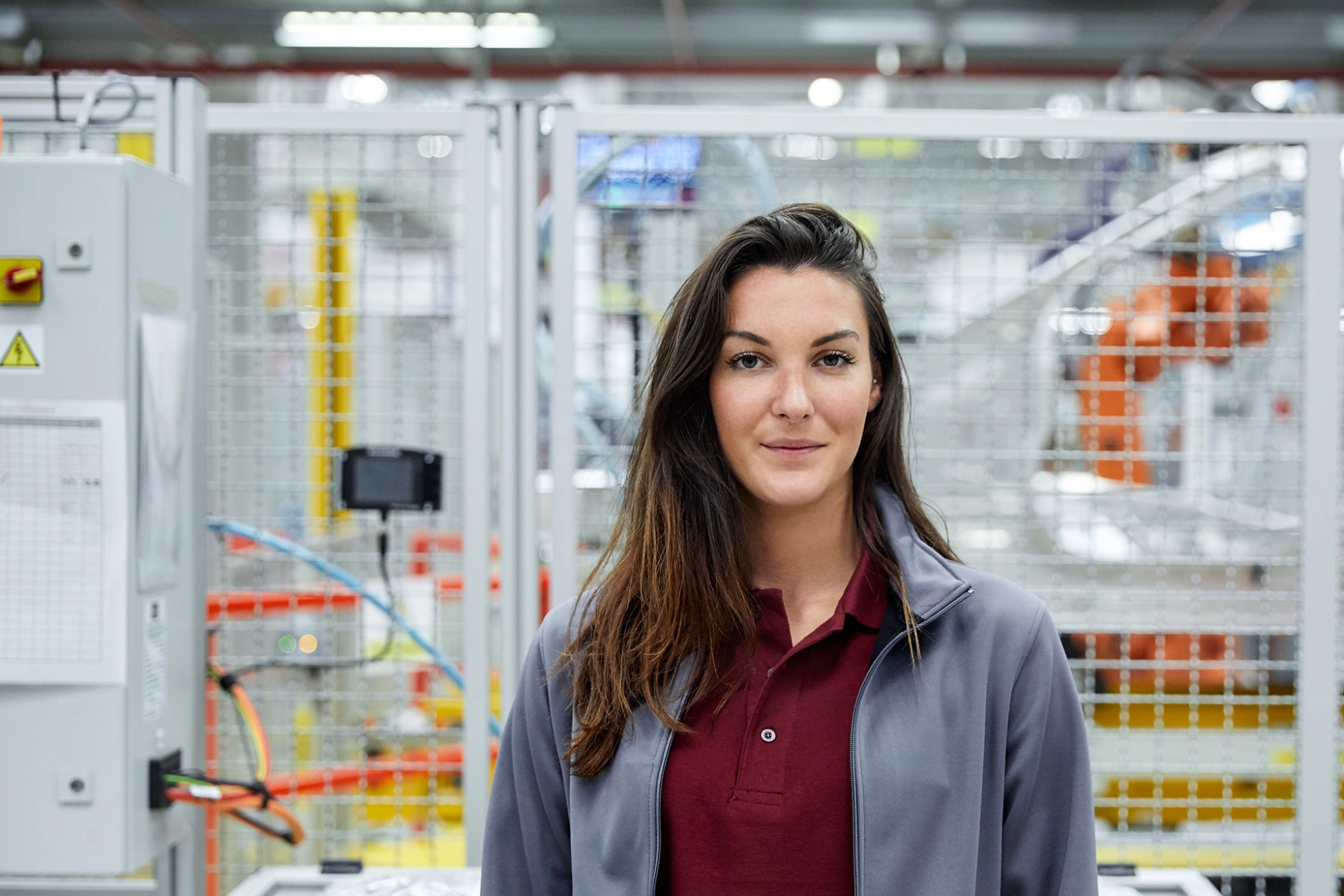 Junge Ingenieurin in der Automobilindustrie steht in der Werkhalle und blickt direkt in die Kamera.