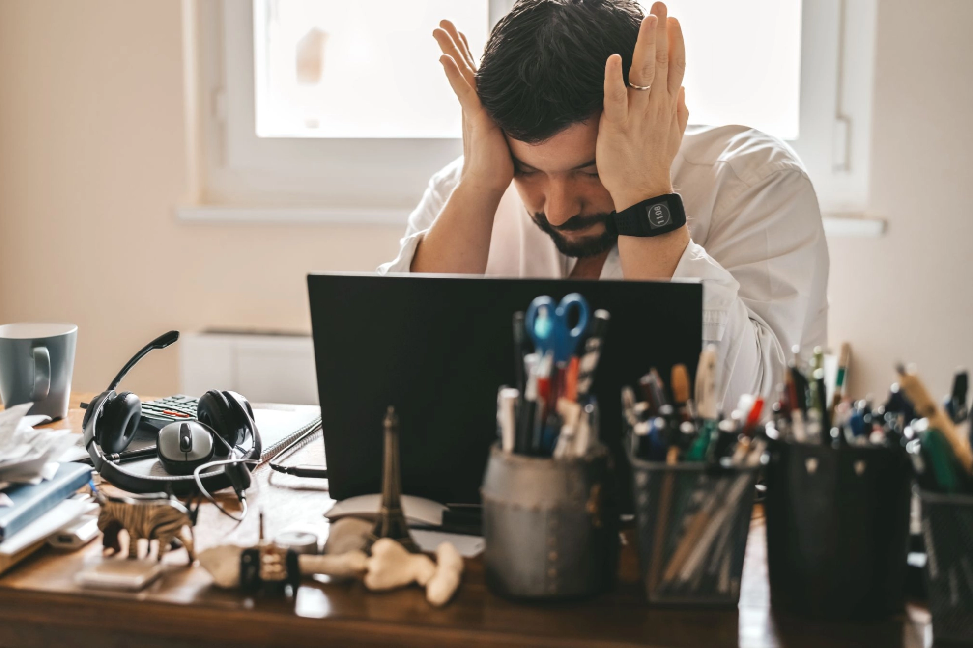 Beschäftigter im Homeoffice legt sich sichtbar gestresst die Hände vor die Stirn.