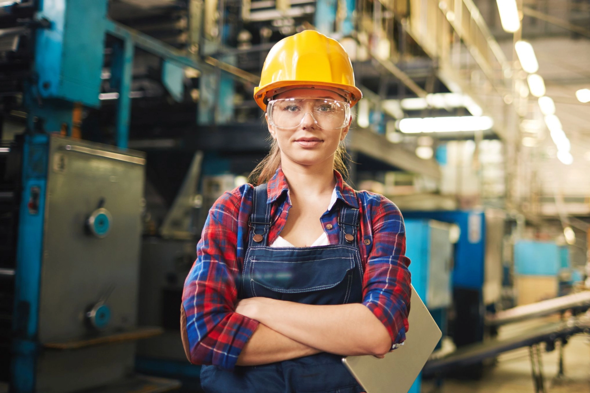 junge Frau mit Arbeitshelm steht in einer Fabrikhalle