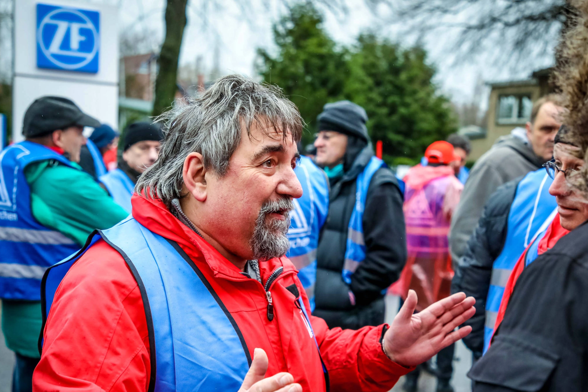 Ein Mann in einer blauen Streikeste im Gespräch mit einem anderen Mann.