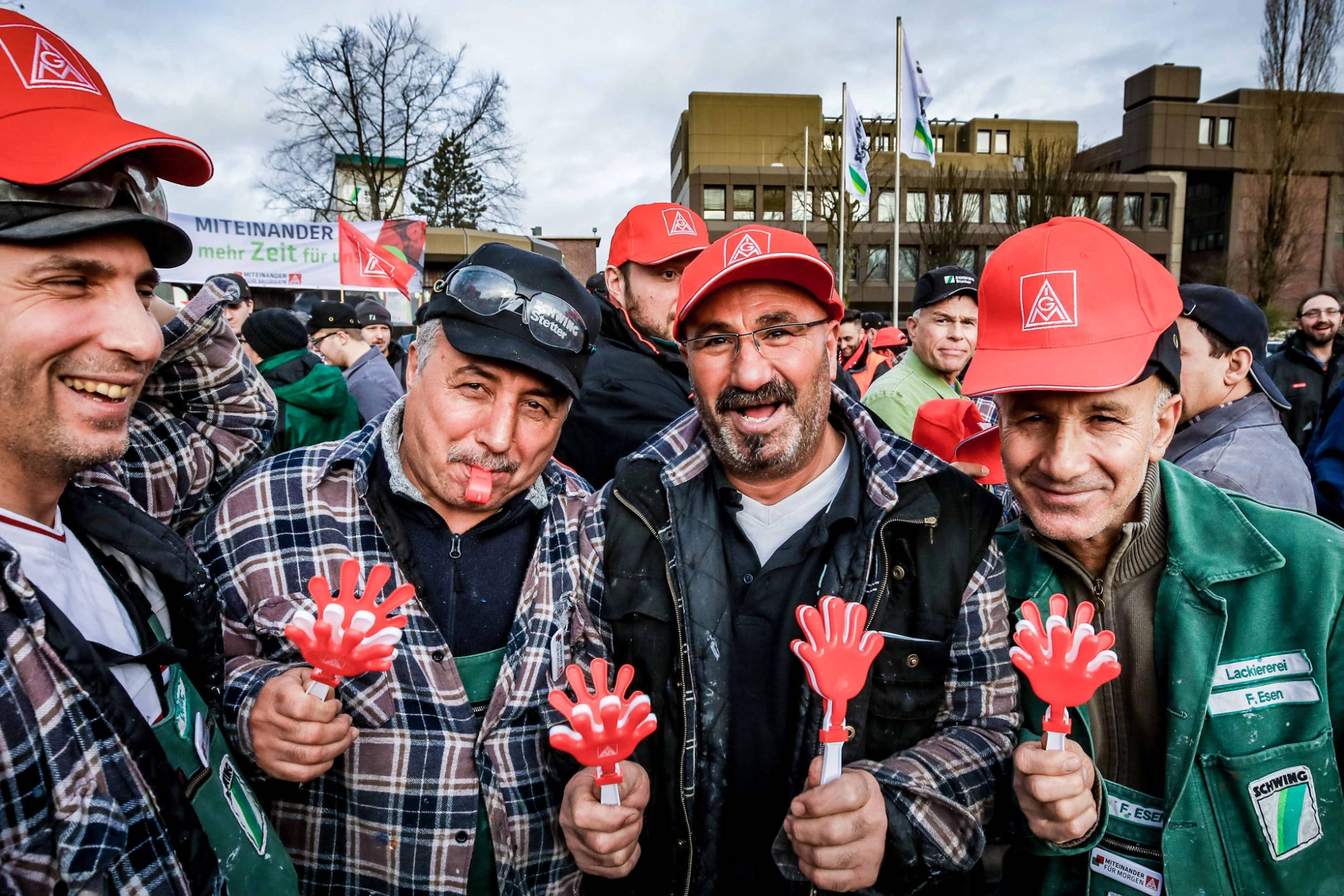 Lachende Männer in Arbeitskleidung und IG Metall-Kappen.