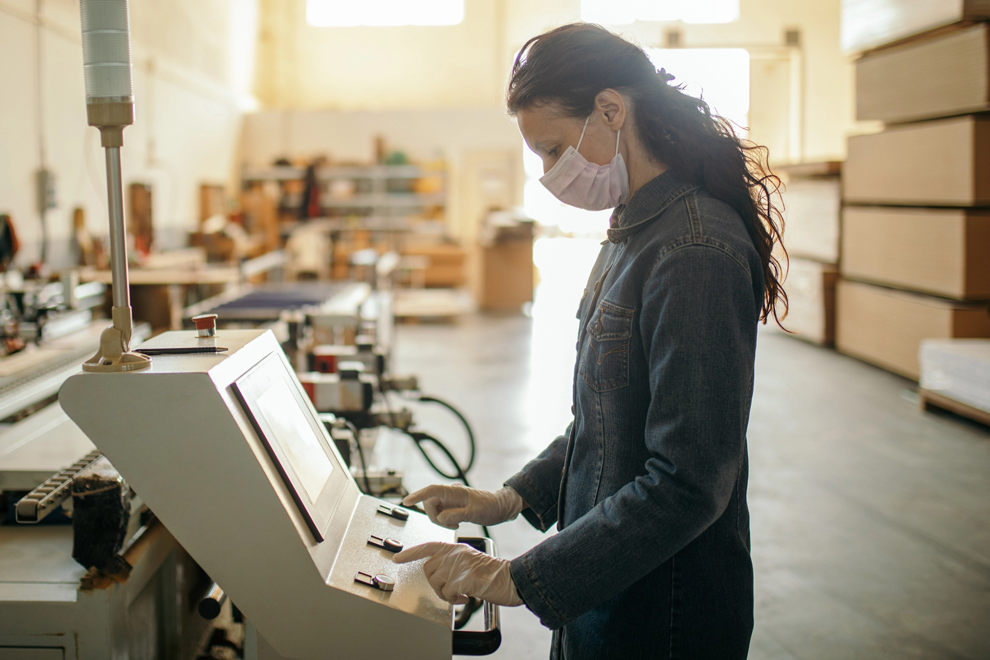 Frau arbeitet mit Mundschutz in einem Industriebetrieb an einer Maschine
