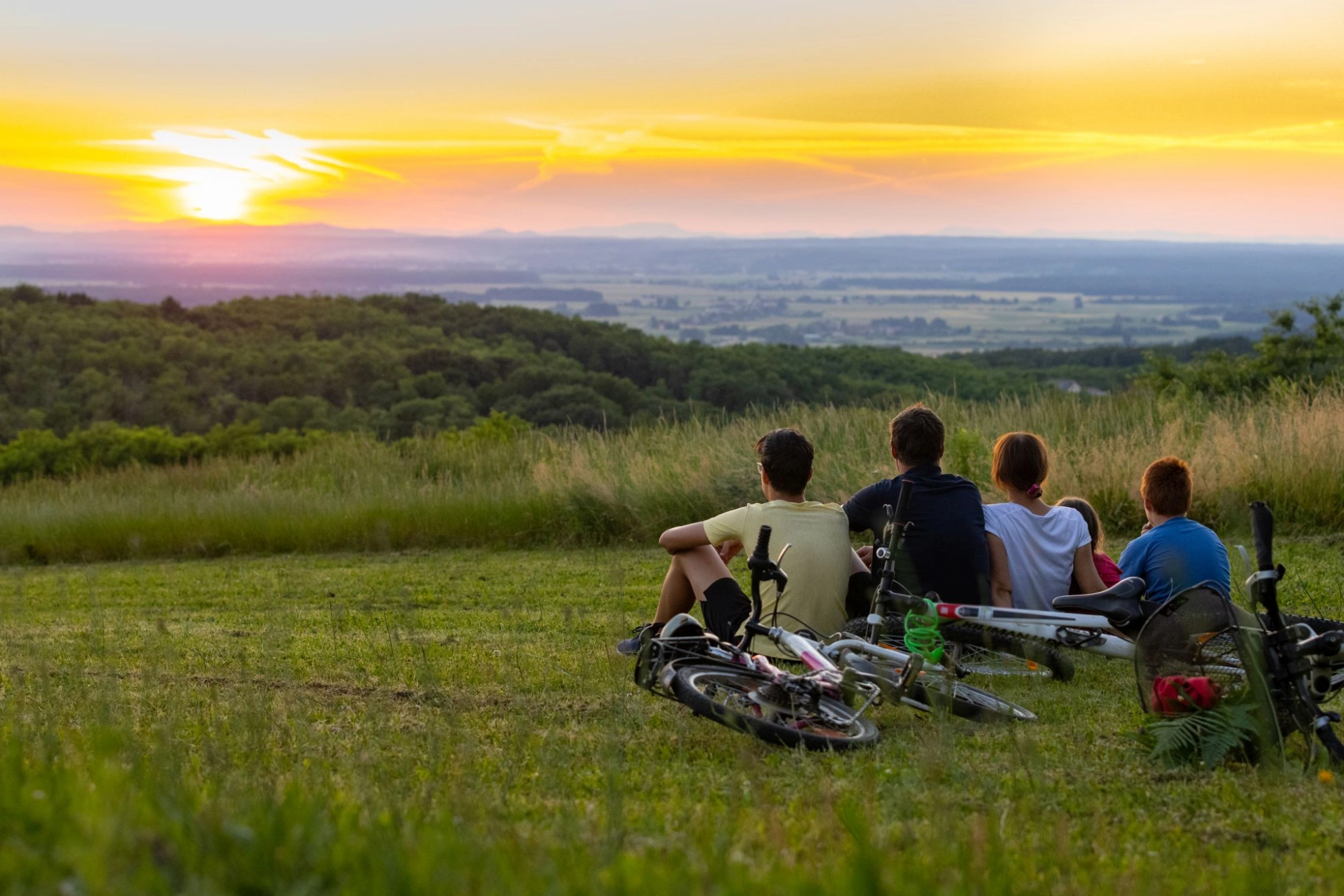 Familie, die nach einer Radtour auf einem Hügel sitzt und den Sonnenuntergang betrachtet 
