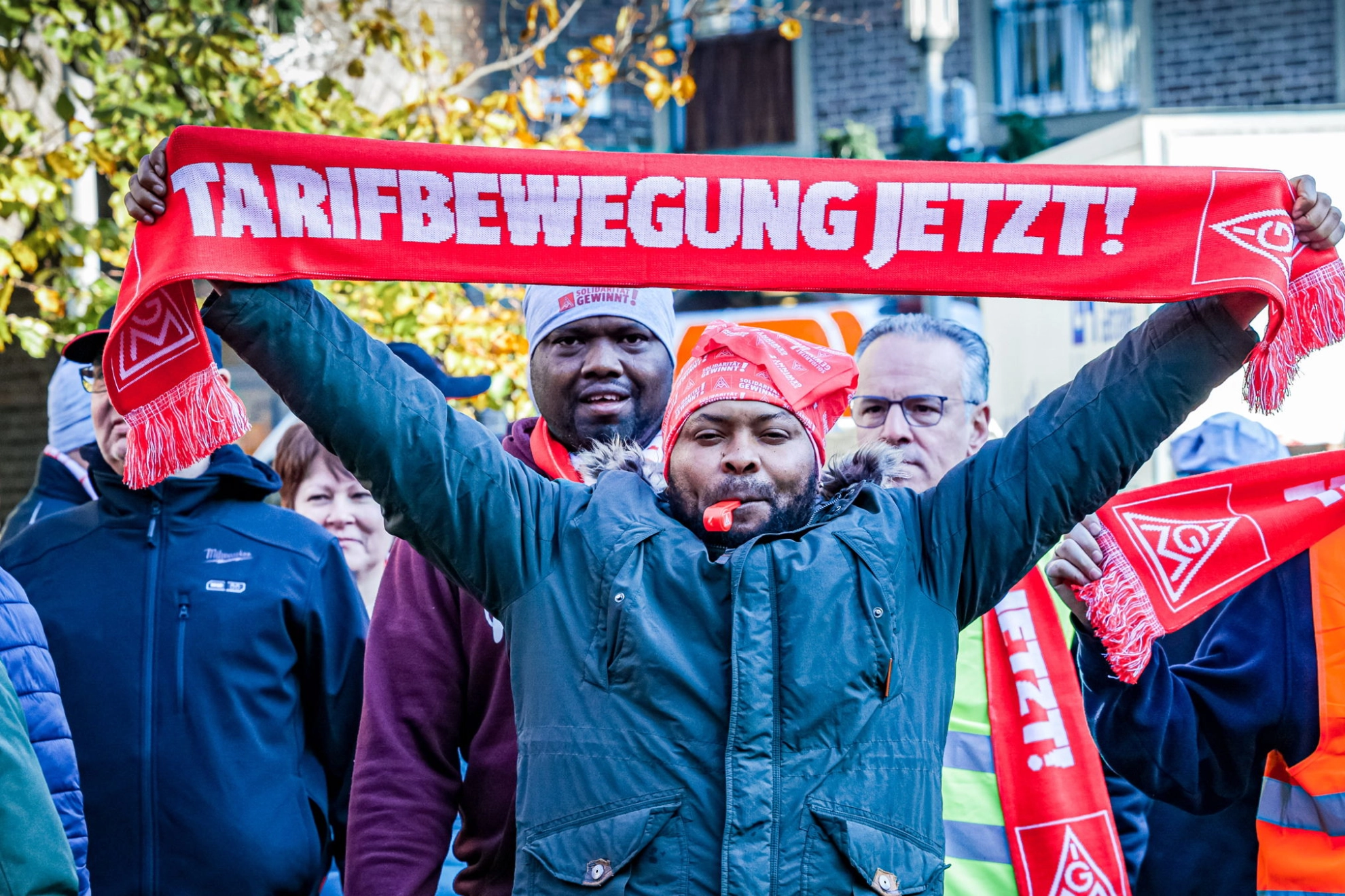 Ein Mann hält einen Schal mit der Aufschrift „Tarifbewegung jetzt“ hoch.
