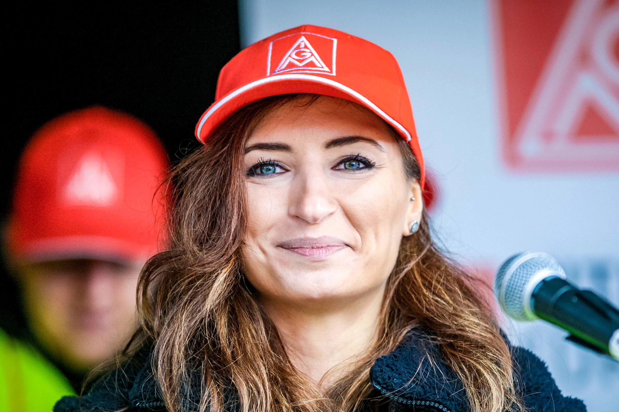 Eine Frau mit langem braunem Haar und IG Metall-Kappe blickt lächelnd in die Kamera.