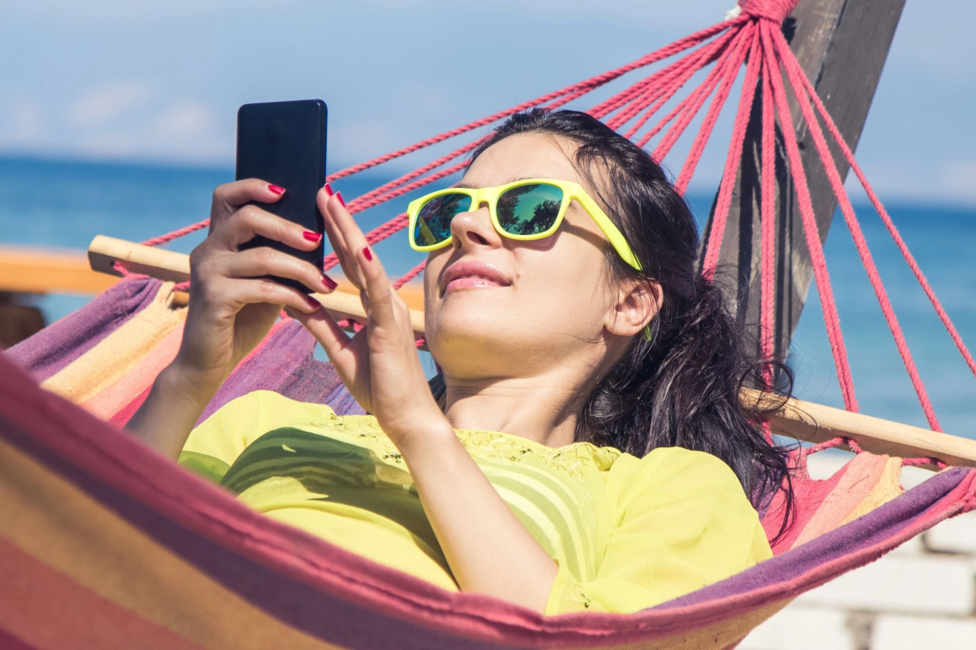 Junge Frau liegt mit ihrem Smartphone in einer Hängematte