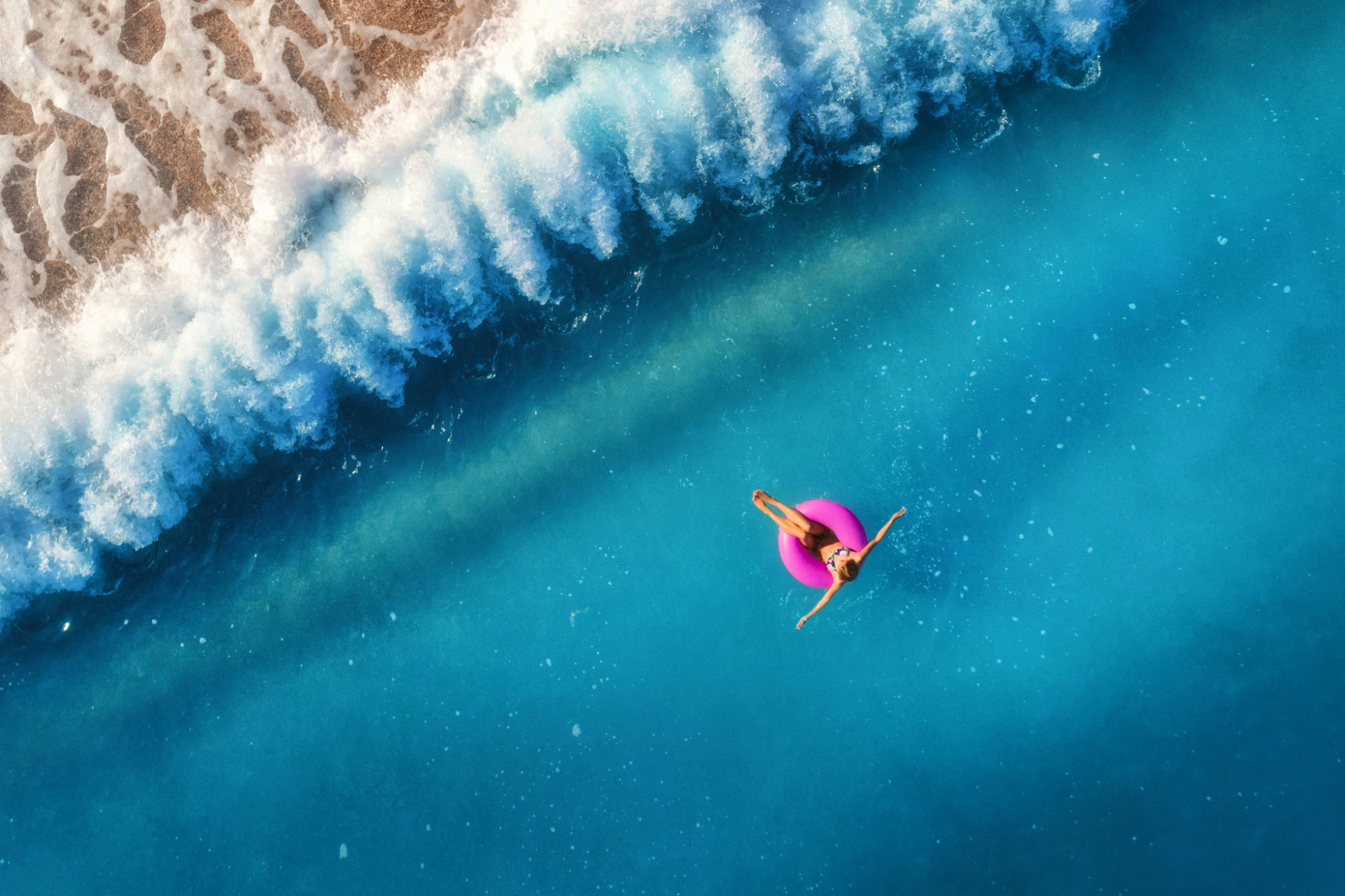 Eine Frau schwimmt auf einem pinken Schwimmring im Meer.
